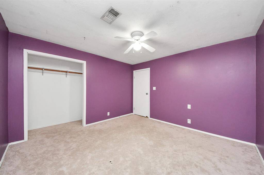 This room features purple walls, a ceiling fan, and a spacious closet. It has neutral carpeting and a simple, clean layout, ideal for personalizing.