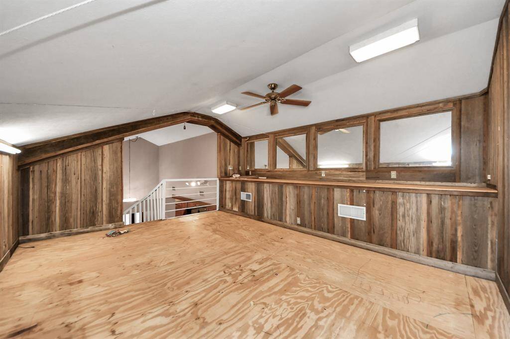 This photo features a rustic loft space with wood paneling and a ceiling fan. It overlooks a staircase with a view of the room below, providing an open and airy feel. Ideal for a cozy retreat or additional living area.