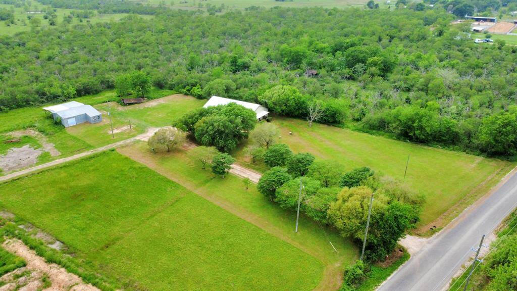 This photo shows a spacious rural property with two large structures, surrounded by greenery and trees. The land is mostly open with clear boundaries, and a road provides easy access. Ideal for those seeking tranquility and space.