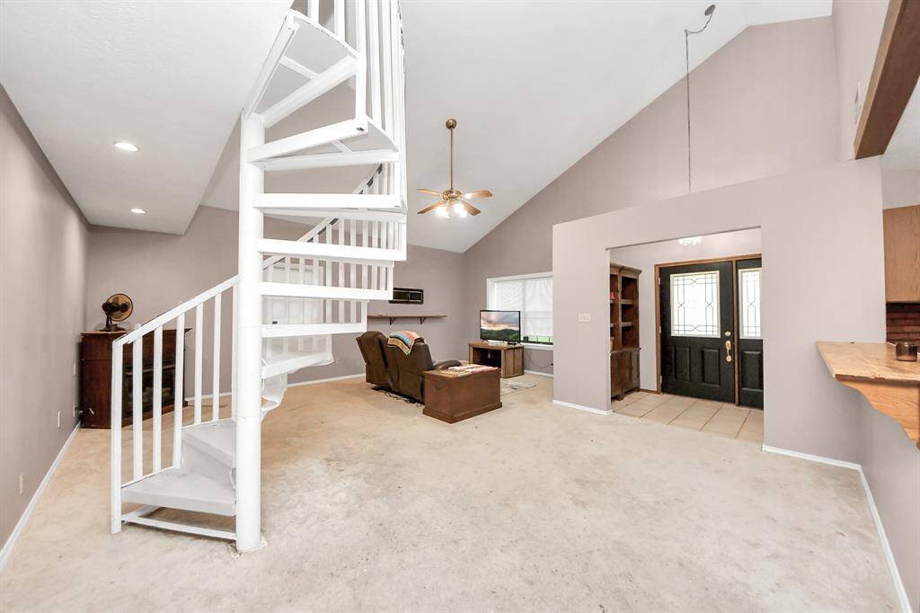 This spacious living area features a high ceiling and a white spiral staircase, offering a modern feel. It includes a cozy seating area and is connected to the entryway with elegant double doors.
