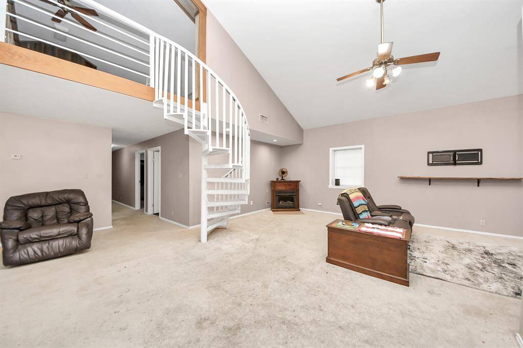 This spacious living area features high ceilings, a spiral staircase leading to a loft, neutral walls, and carpet flooring.