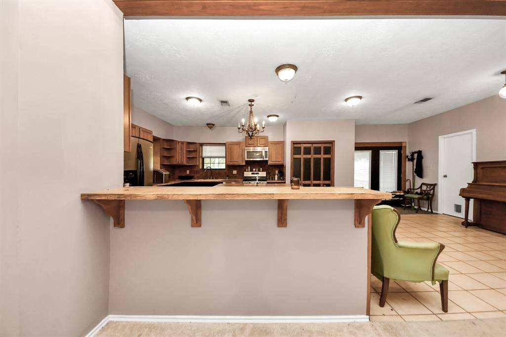 Spacious open-concept kitchen and living area featuring a wooden breakfast bar, stainless steel appliances, and ample cabinetry. The area is well-lit with a chandelier and recessed lighting, and includes a cozy seating space with tiled flooring.