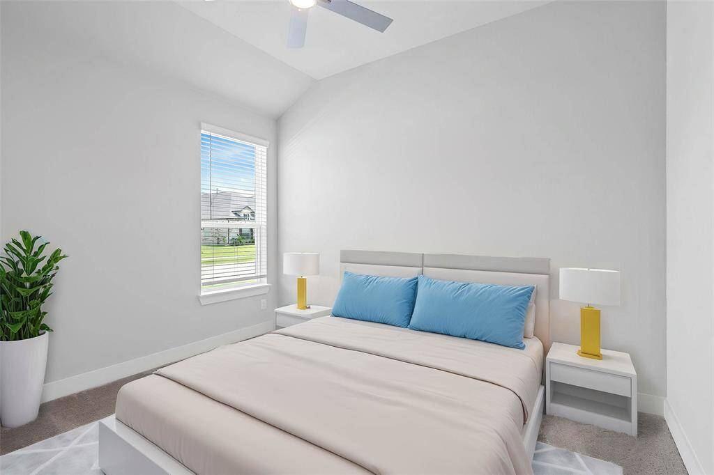 Secondary bedroom features plush carpet, custom paint, ceiling fan, closet space, and a large window with blinds.