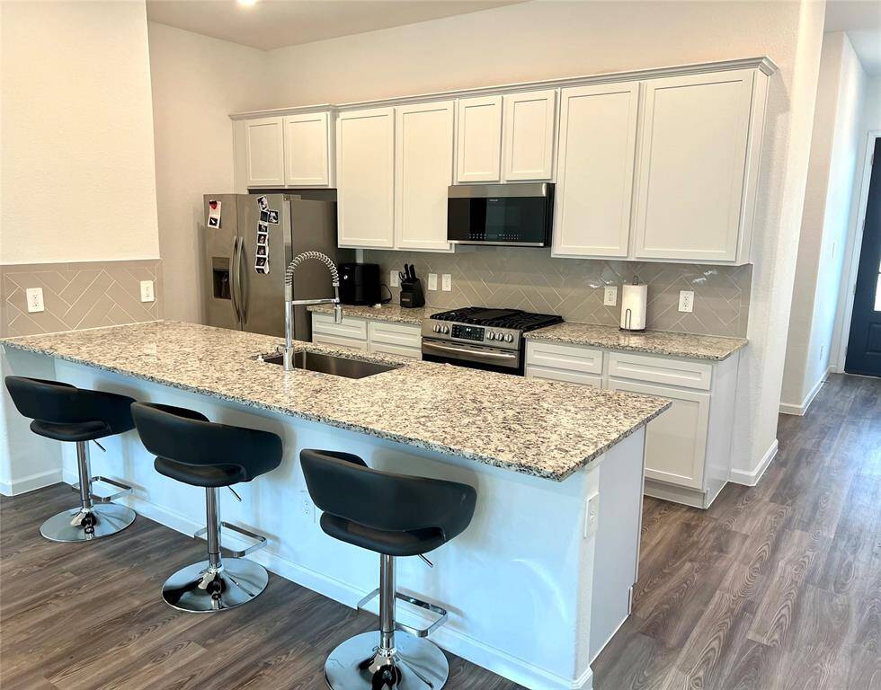 Kitchen features shaker style white cabinets, breakfast bar, stainless steel appliances and a modern herringbone backsplash.