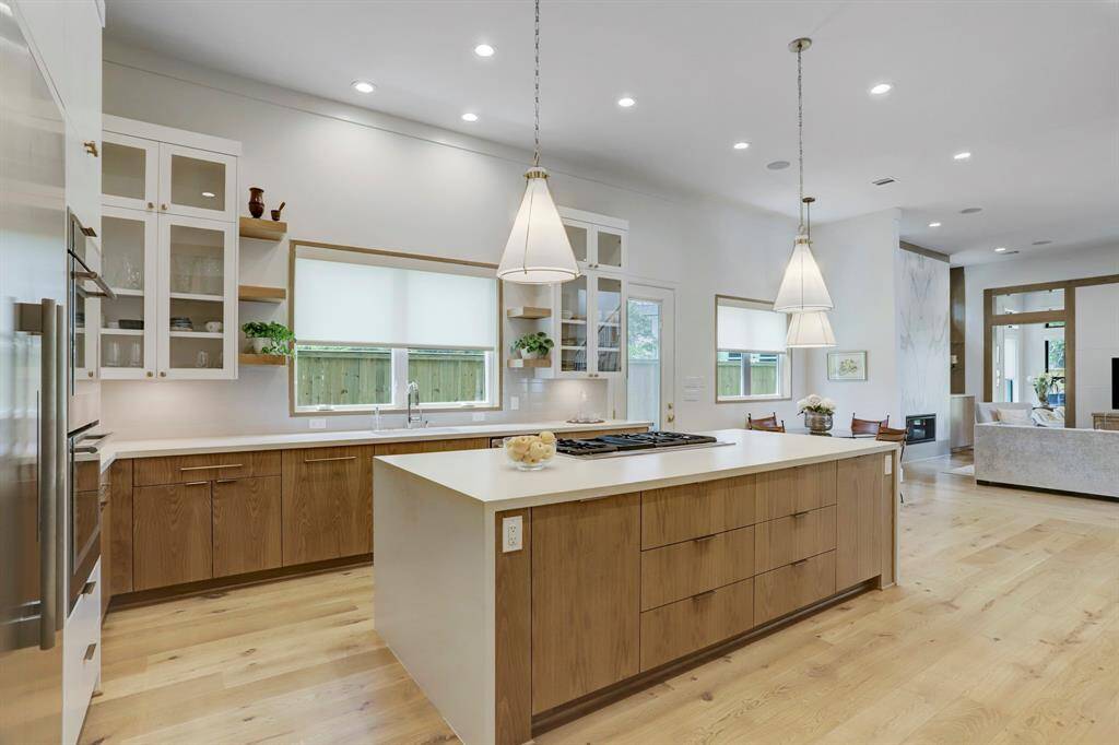 Extra details throughout the kitchen include a Quartz waterfall counter top at the island, upper glass cabinetry, floating wood shelves flanking the wood cased window. All wood cabinetry has a custom stain.