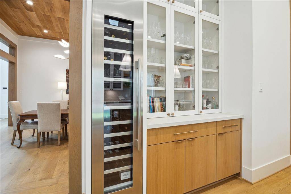 Thermador Tall 18” Wine Refrigerator sits adjacent to the custom finished cabinets including quartz counter top and upper glass display cabinets.