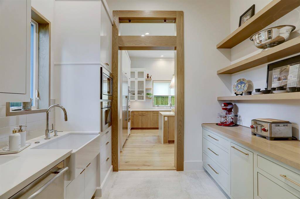 This is a pass-through working butler pantry with a secondary dishwasher, apron sink with quartz countertop, microwave, and Thermador coffee machine on one side. On the opposite wall a wood counter top adds extra character to custom cabinetry along with matching floating wood shelving.  The perfect storage for all our extra small appliances and serving pieces.