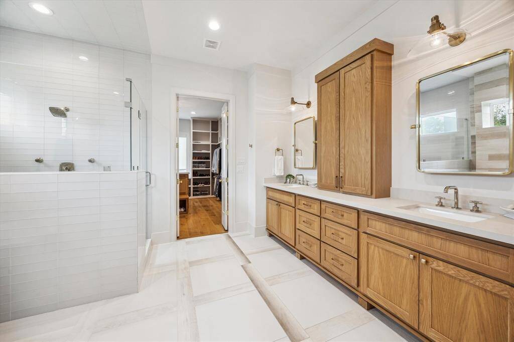 Custom-built wood cabinetry with quartz countertops, porcelain tile with wood inlay detail for the flooring,  a floating tub with nickel-finish hardware, an oversized shower with frameless glass enclosure, nickel hardware, and jet sprayers are just a few of the high-level finishes used in this spa-like primary bath.