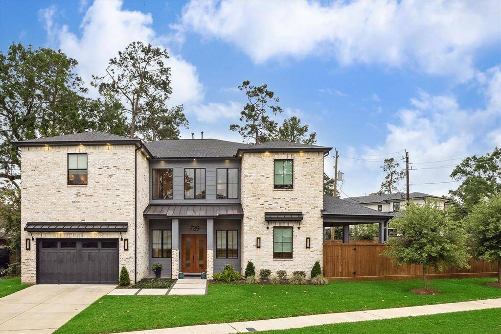 It features a sleek, modern facade with a solid mahogany double-door entry, Hardi-plank siding and white/grey brick, a black composition shingle roof, and black metal accent awnings.