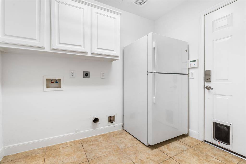 The laundry room features, a refrigerator, and white cabinets.