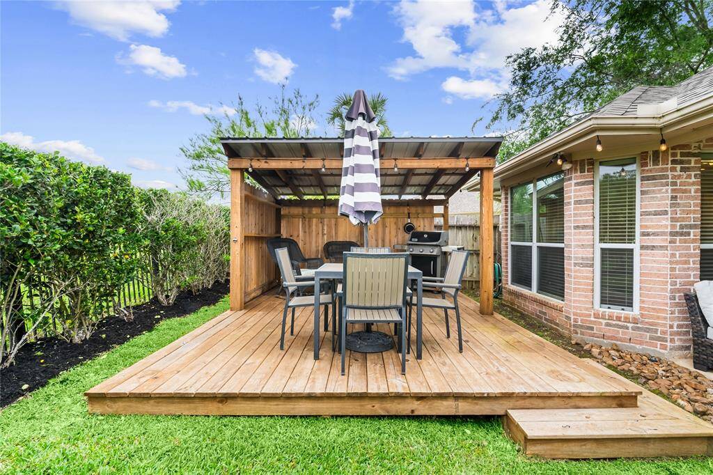 Charming backyard deck with a covered pergola, outdoor dining set, grill station, and string lights—perfect for relaxing or entertaining.