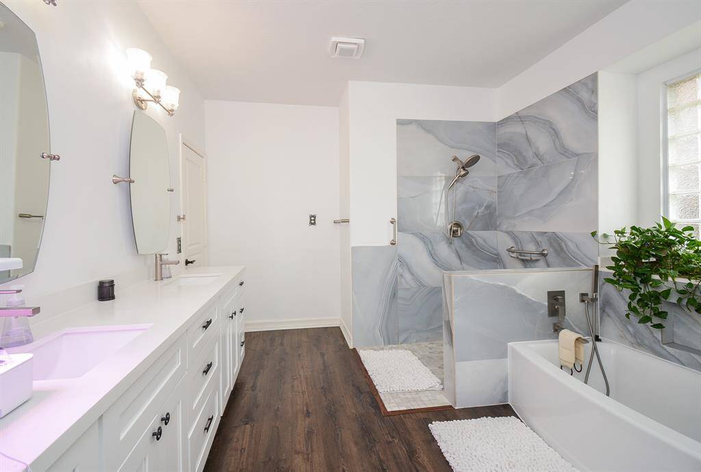 A bright modern vibe embraces this ensuite bath; with traditional cabinetry; gorgeous steel gray shower tiling, and long, soaking tub, right.
