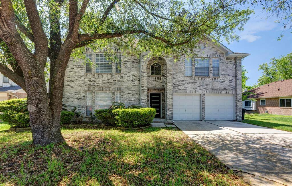 Stately two-story brick home with charming curb appeal, featuring a mature tree and spacious two-car garage.