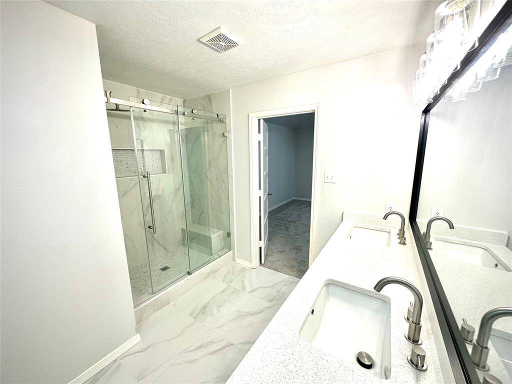 This modern bathroom features a sleek glass-enclosed shower with a rainfall showerhead, a compact vanity with a stylish mirror, and a contemporary toilet, all set against elegant marble-look tiles.