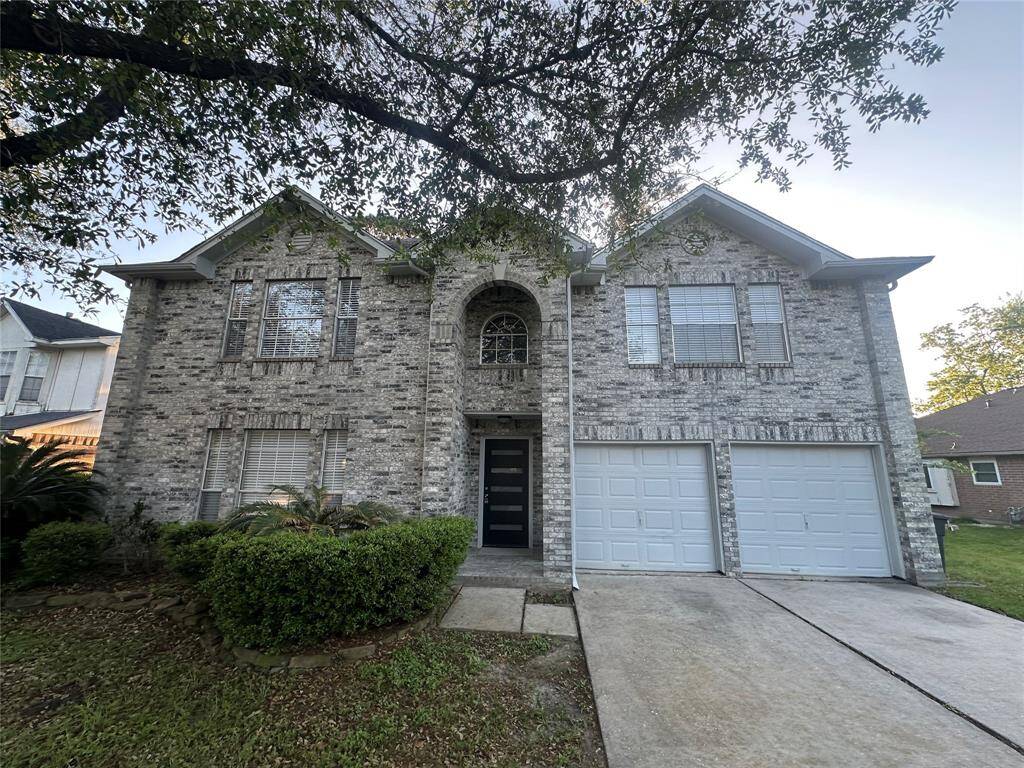This two-story brick home features a double garage, a symmetrical facade with multiple windows, and a well-maintained front yard with mature trees.