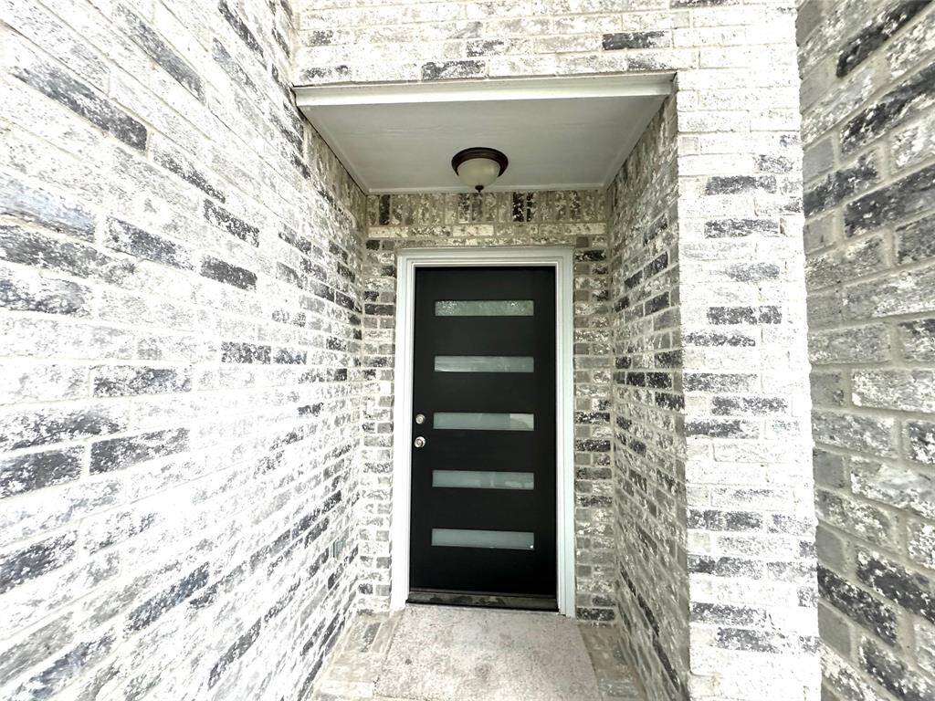 Modern entryway featuring a sleek black door with horizontal glass panels, set against a distinctive light gray brick exterior.