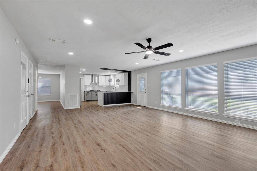 This spacious room features light wood flooring, neutral walls, a ceiling fan, and modern lighting. A staircase leads to the upper level, and a window provides natural light. Ideal for a living or dining area.