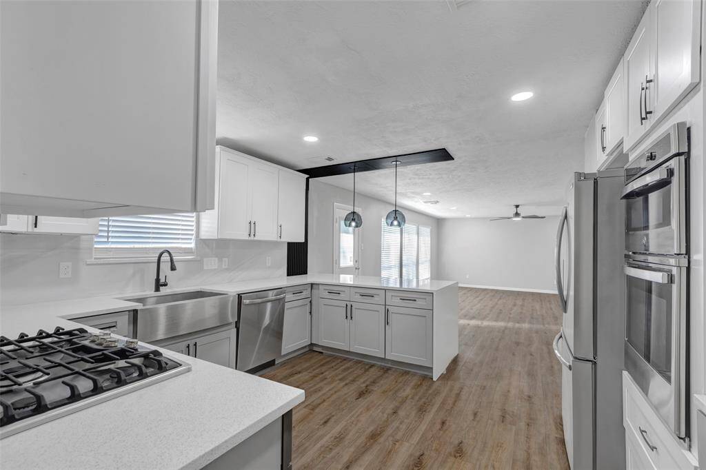 This photo shows a bright laundry room and pantry with built-in shelving and hookups for appliances. It has light wood flooring and a clean, modern look.