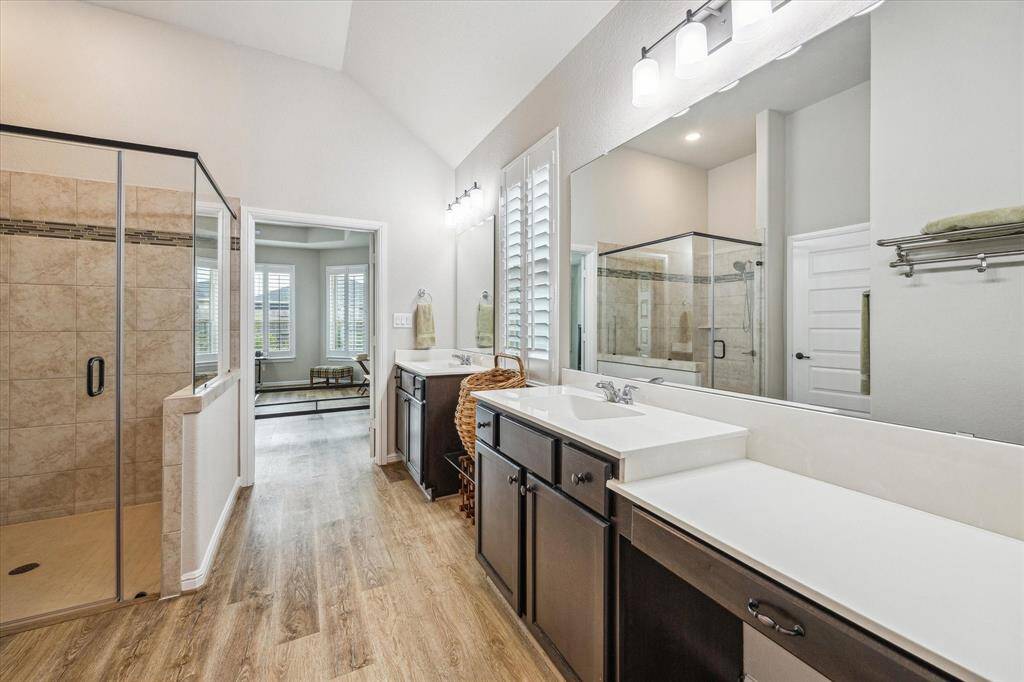Primary suite has an oversized glass shower with tile and inlay tile design, separate water closet with even an extra cabinet over the toilet, grab safety bars, and vaulted ceiling.
