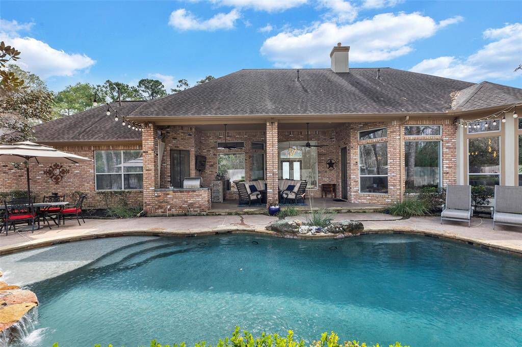 This photo showcases a charming brick house with a spacious backyard featuring a beautiful pool. The patio area includes seating and a dining set under an umbrella, ideal for outdoor relaxation and entertaining. Lush greenery surrounds the space, enhancing its inviting atmosphere.
