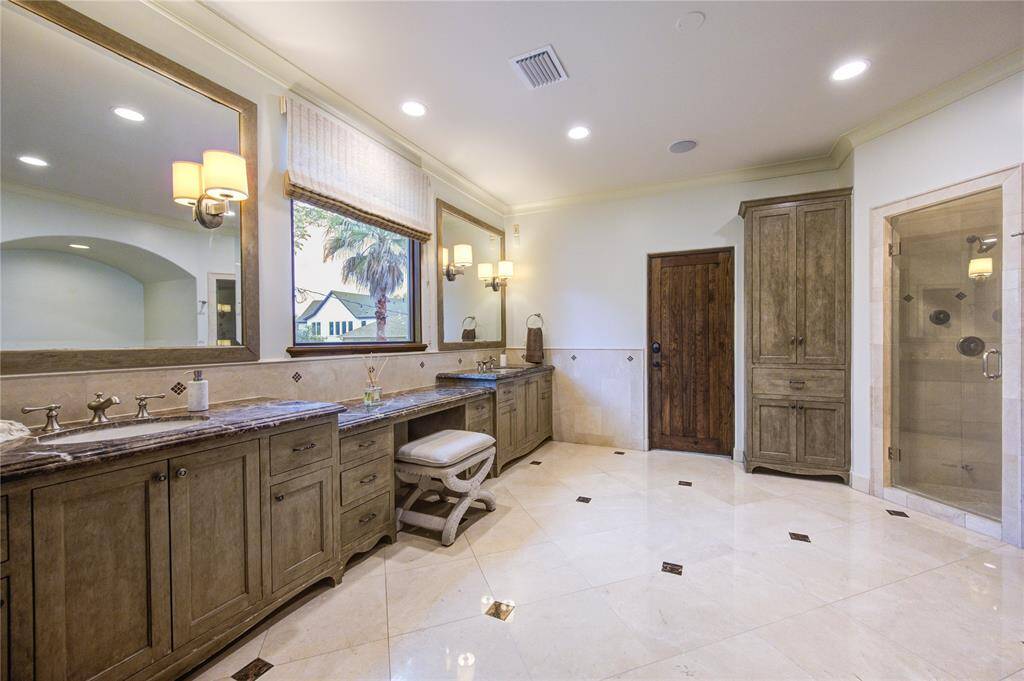 This Awesome spacious primary bathroom features elegant marble tile flooring, a large dual-sink vanity with loads of storage, and a glass-enclosed shower.