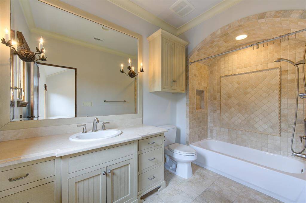 This elegant ensuite bathroom features a large mirror with stylish sconces, a spacious vanity, and a bathtub with a tiled shower area.
