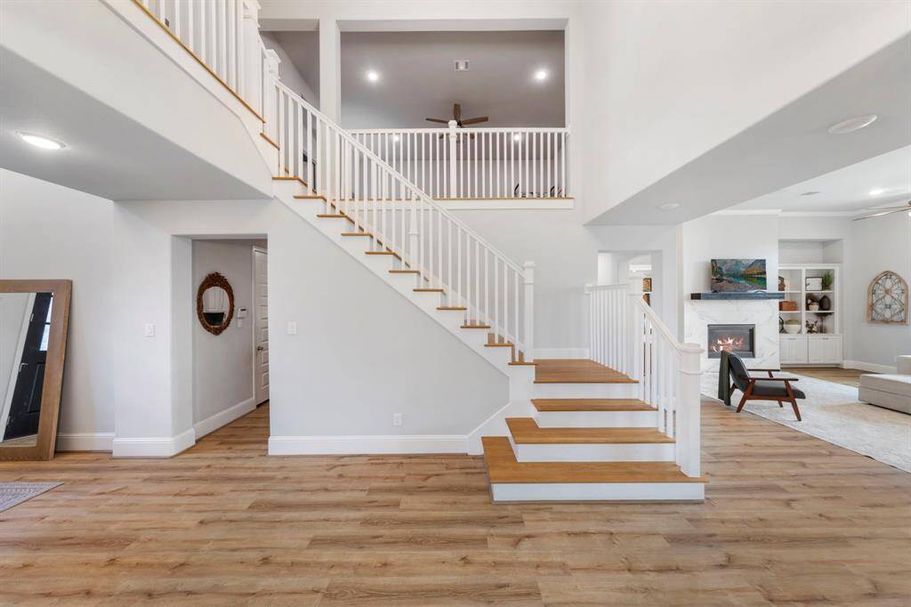 Striking entryway with soaring ceilings, elegant wood-accented staircase, and luxury vinyl plank flooring, seamlessly leading into the open living space.