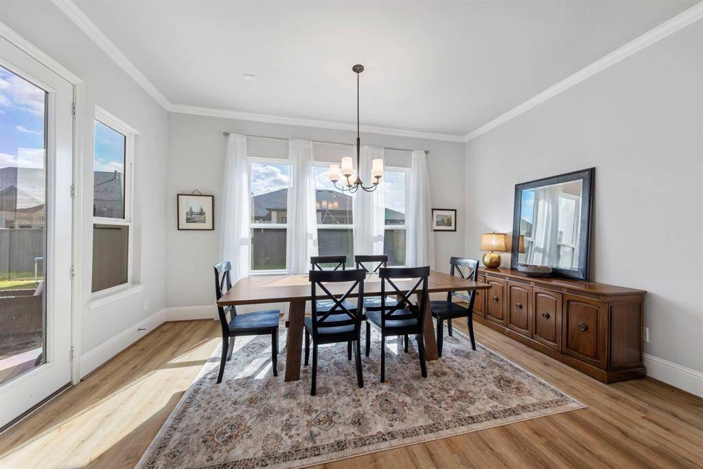 The breakfast room is filled with natural light from expansive windows, complemented by high ceilings, elegant crown molding, and luxury vinyl plank flooring. Upgraded window tint keeps the space cool in summer without compromising brightness!