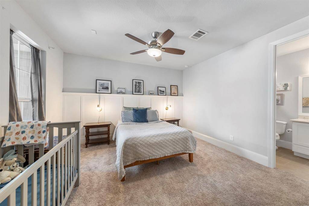 First-floor guest suite with ensuite bath, ideal for guests or multigenerational living. Features wood-paneled accent wall, cozy carpet, and plenty of natural light.