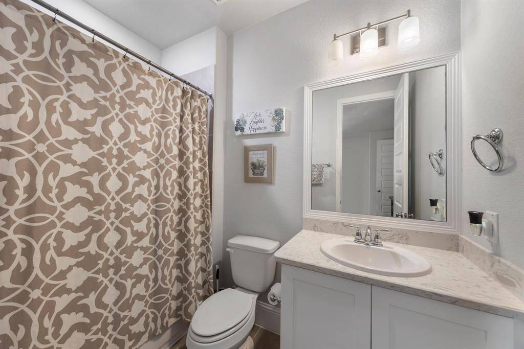 First-floor bedroom with ensuite bath, featuring a framed mirror, quartz countertops, and timeless tile shower and flooring.