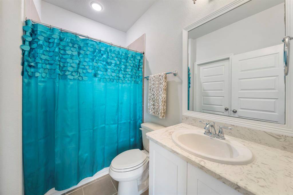 Second-floor bedroom includes an ensuite bath and walk-in closet, featuring a framed mirror, quartz countertops, and tile flooring.