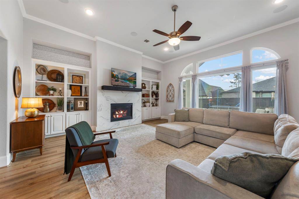 Elegant living room features a cozy fireplace with a sleek marble surround, built-in shelving, and oversized windows that fill the space with natural light.