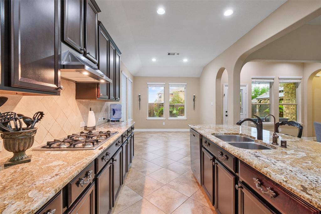 Cook and connect in this chef-style kitchen featuring granite countertops, dark cabinetry, and bronze fixtures. Enjoy filtered, softened water thanks to the FilterSmart whole-home tankless water system—no salt needed!