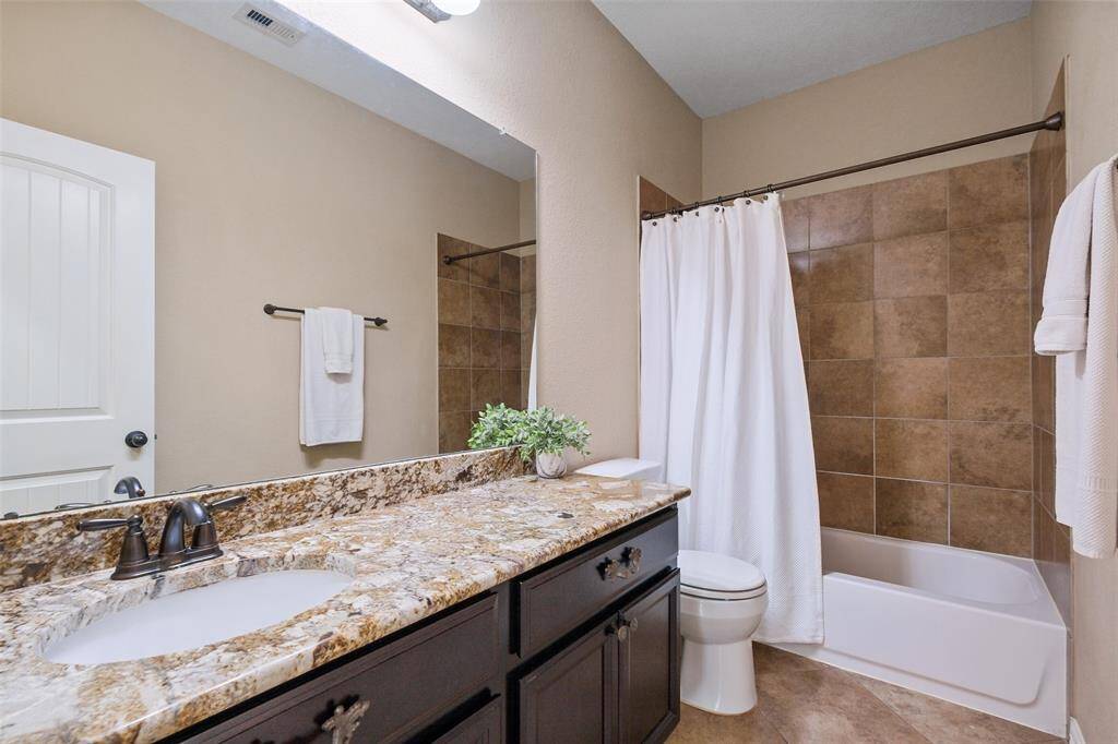 This full bathroom offers warm-toned tilework, granite countertops, and a tub-shower combo—perfect for guests or everyday use. Its neutral palette complements the rest of the home beautifully while delivering both function and style.