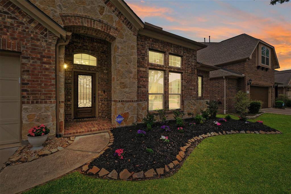 A closer look at the charming entryway—brick archway, elegant iron front door, and flower beds blooming with color. This is your invitation home.