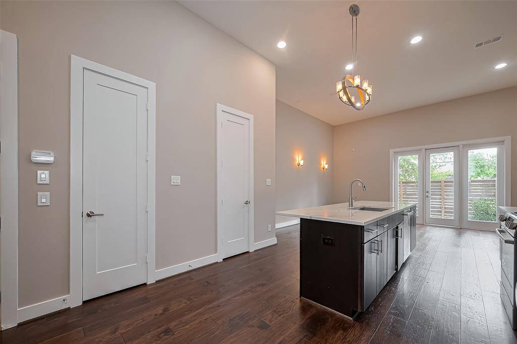 Over the kitchen island hangs a stylish modern chandelier or pendant light fixture, adding a sleek touch to the space. On the opposite wall, two doors provide convenient access—one leads to a coat storage closet, while the other opens to a well-placed half bathroom, perfect for guests.