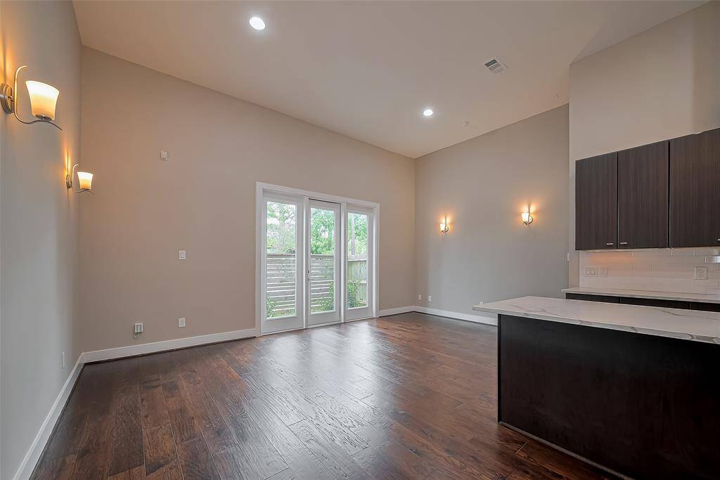The kitchen seamlessly flows into a spacious 1st-floor living room (19.4 x 12.0) with a dramatic 13-ft ceiling and recessed lighting. Dual sets of wall sconces on each side provide soft, ambient illumination, enhancing the room's inviting atmosphere. Full-light windows and a door lead to the fenced backyard, offering a perfect transition for indoor-outdoor living and plenty of natural light.