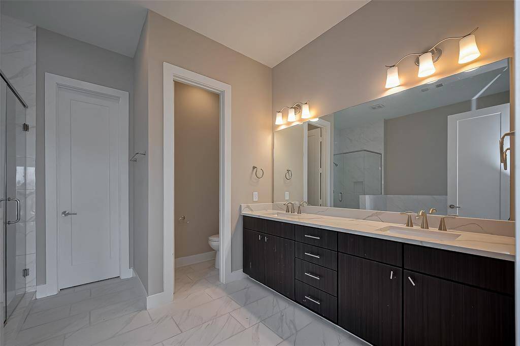 The owner's ensuite bathroom features a long vanity with two rectangle-shaped undermount sinks, complemented by a quartz countertop. Ample storage is provided with four drawers between the sinks. A long wall mirror and over-mirror lighting enhance the space, while a private water closet houses the commode for added privacy. The tile floors complete the sleek, modern design.