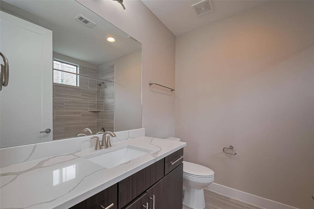 Bedroom #2’s ensuite bathroom (8.2 x 7.1) features a rectangle-shaped undermount sink in a quartz vanity with two drawers for storage. A wall mirror and over-mirror lighting brighten the space. The combination tub and shower are accented with tiled shower walls, while a window above the tub allows natural light to fill the room. Additionally, the bathroom includes a linen closet for added storage and convenience.