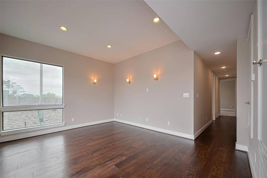 The staircase to the 3rd floor leads to a spacious gameroom, two bedrooms, and a full bathroom. Both the gameroom and hallway feature elegant engineered wood floors, complemented by recessed lighting and wall sconces that enhance the ambiance. Large windows throughout fill the space with abundant natural light, creating an inviting and airy atmosphere perfect for relaxation or entertainment.