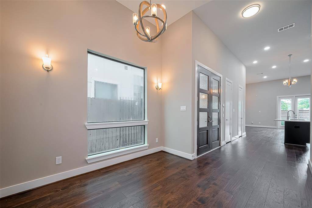 The double front doors open to a spacious first floor with soaring 13-ft ceilings. To one side, a formal dining room is framed by a large window overlooking the entry walkway, flanked by modern wall sconces for added elegance. A sleek, updated chandelier adds a stylish focal point. On the opposite side, the open-concept island kitchen flows seamlessly into the living room, creating a bright and inviting space for everyday living and entertaining.