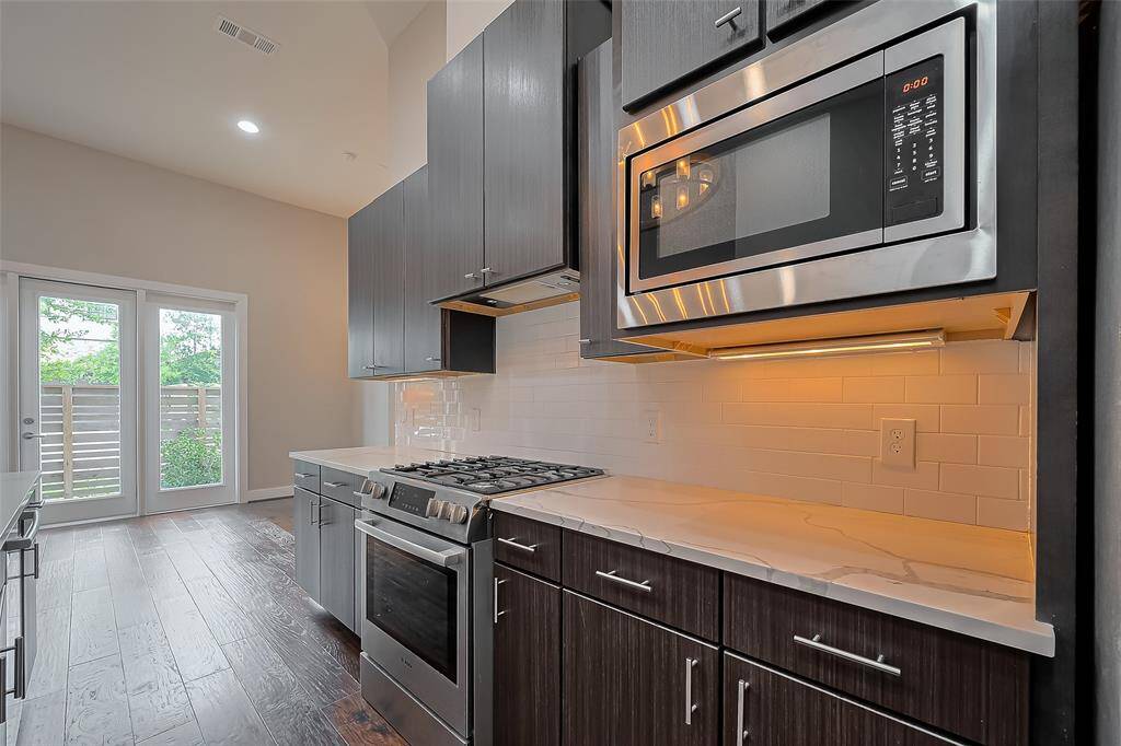 The kitchen is equipped with a stainless steel Bosch 5-burner gas range—perfect for those who appreciate the precision and power of gas cooking. A sleek stainless vent hood adds both function and style, while an elevated Whirlpool microwave helps maximize valuable countertop space. Under-cabinet lighting enhances visibility and adds a warm, modern touch to this well-appointed culinary space.