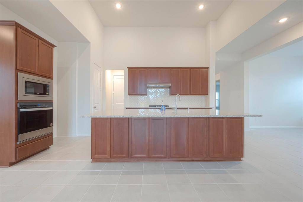 Kitchen features ample cabinets, tile backsplash, granite counters, huge island, and a walk-in pantry.