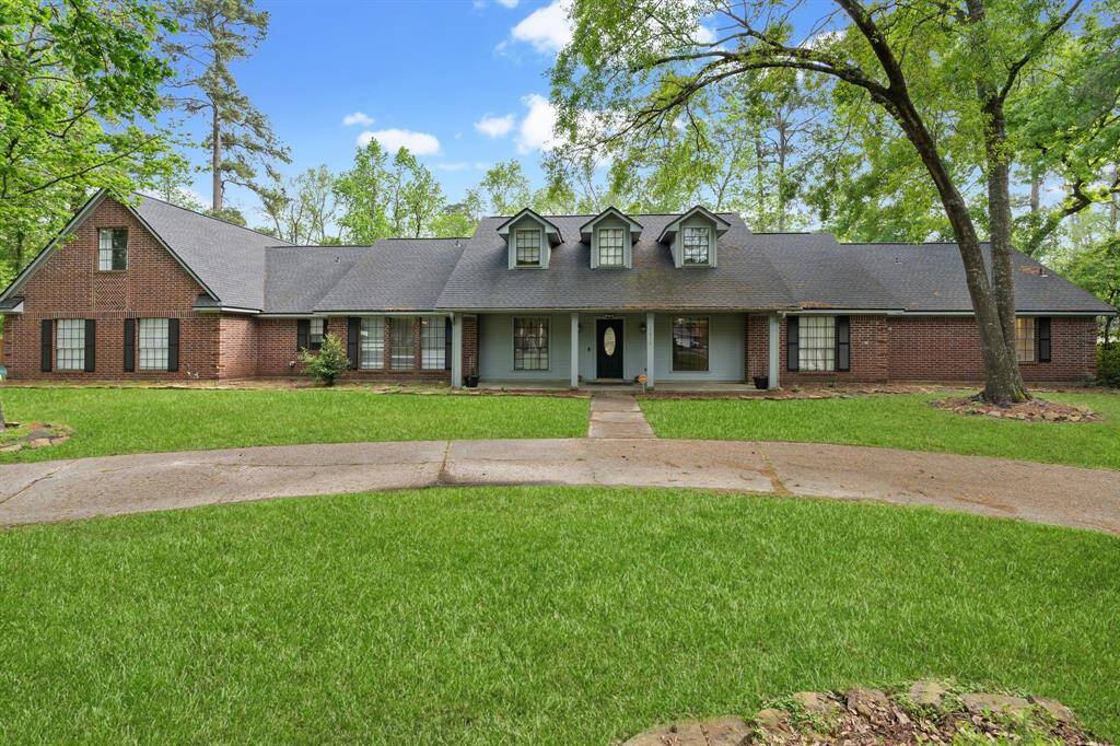 Home is surrounded by lush greenery and features a circular driveway.