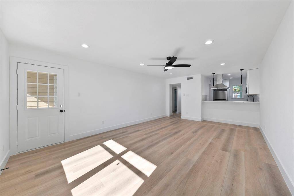 Bright and open living space with modern wood flooring, recessed lighting, and a ceiling fan. The kitchen features sleek finishes and a passthrough window, enhancing the sense of space.