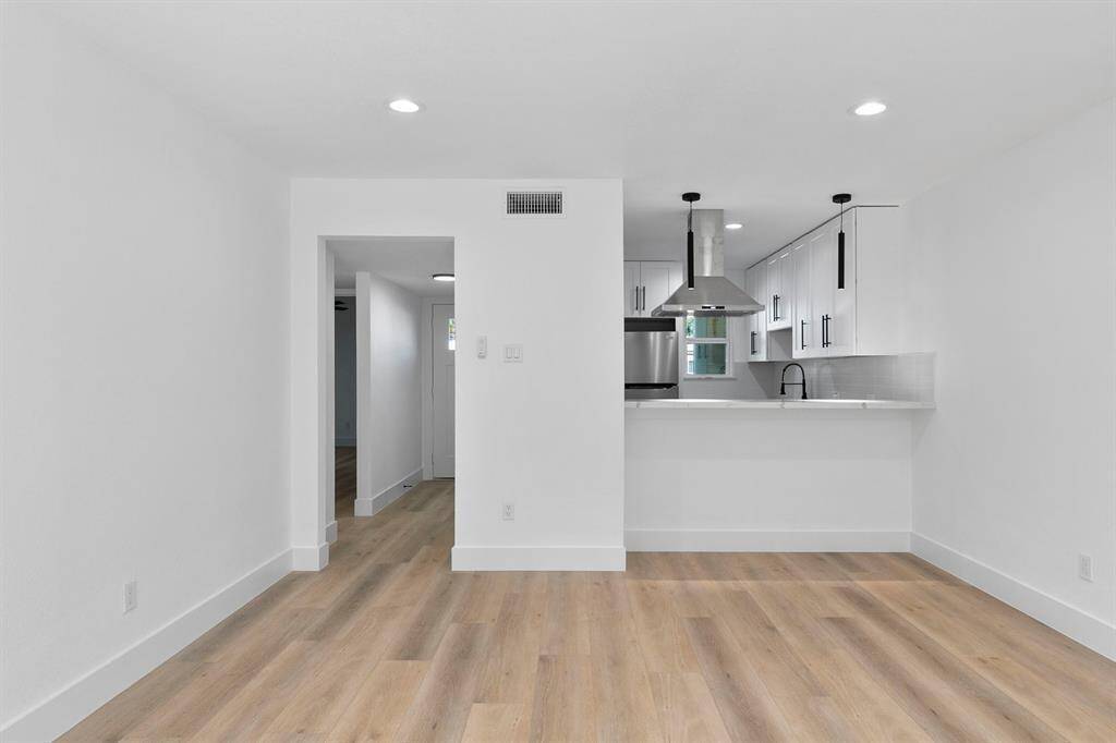 This photo showcases a modern, open-concept kitchen and living area with sleek white cabinetry, stainless steel appliances, and a stylish range hood. The space features recessed lighting and light wood flooring, creating a bright, inviting atmosphere.