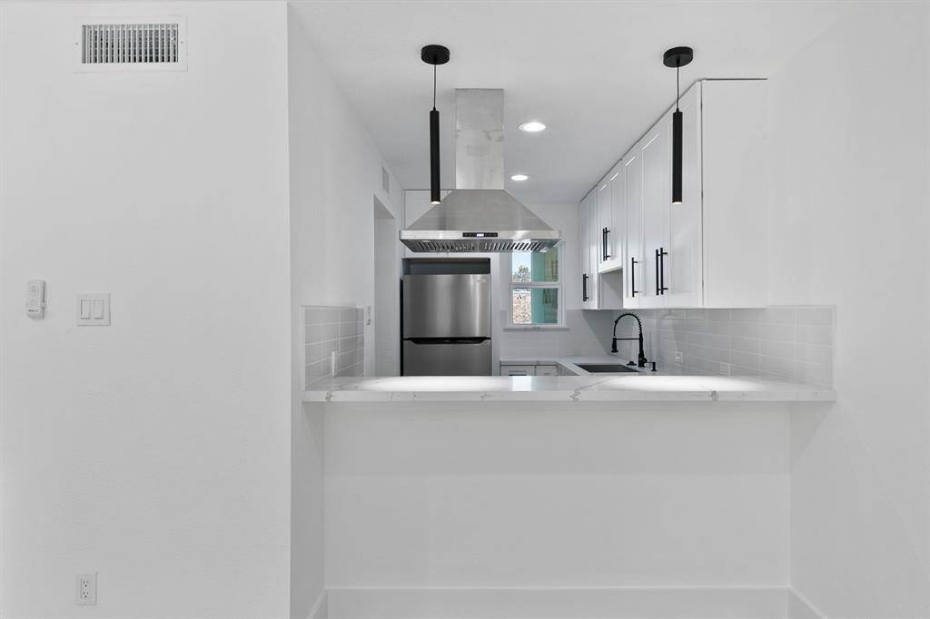 This kitchen features a modern design with sleek white cabinetry, stainless steel appliances, and a stylish island with bar seating. It has a clean, minimalist look with black fixtures and recessed lighting, creating a bright and inviting space.