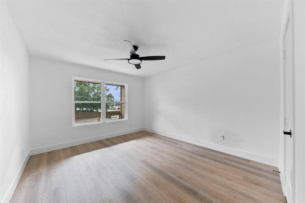 This room is spacious and bright with light wood flooring and a large window offering plenty of natural light. It features a modern ceiling fan and neutral wall colors, creating a clean and inviting atmosphere.