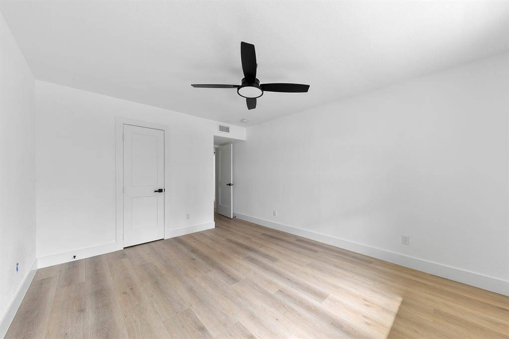 This room features a clean, modern design with white walls, light wood flooring, a black ceiling fan, and ample natural light. It includes a closed door leading to an adjacent space, enhancing functionality.