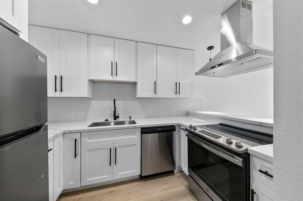 This modern kitchen features sleek white cabinetry with black hardware, stainless steel appliances including a refrigerator, dishwasher, and range hood. It has a clean, minimalist design with bright lighting and a functional layout.